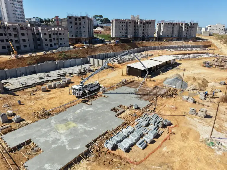Vista aérea de laje de concreto com ferragem exposta, equipe trabalhando, prédios residenciais ao fundo.