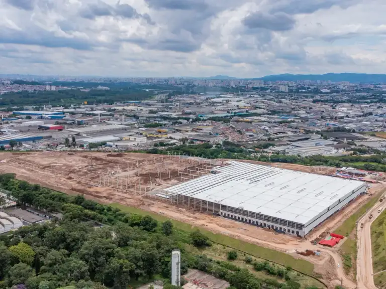 Vista aérea de galpão industrial em fase de cobertura, estrutura metálica parcialmente coberta.