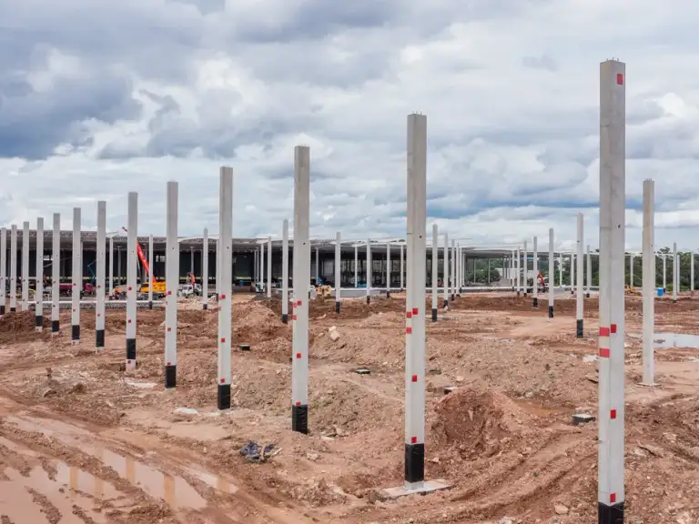 Vista aérea de fileiras de colunas de concreto recém-instaladas em terreno preparado para galpão industrial.