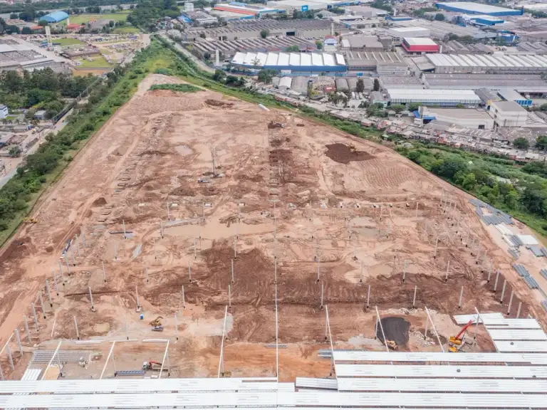 Vista aérea ampla de terreno em preparação para construção, perímetro urbano ao fundo.