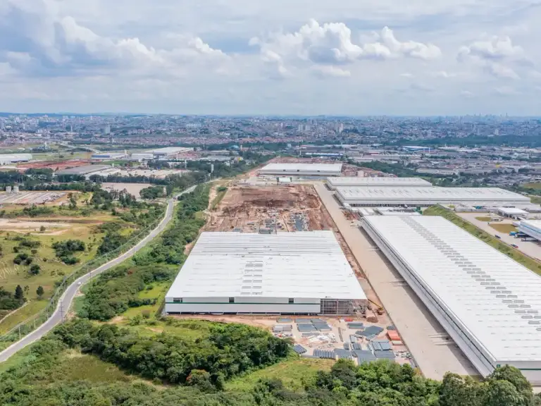 Vista aérea de galpão industrial com cobertura branca concluída, cercado por vegetação e vias de acesso.