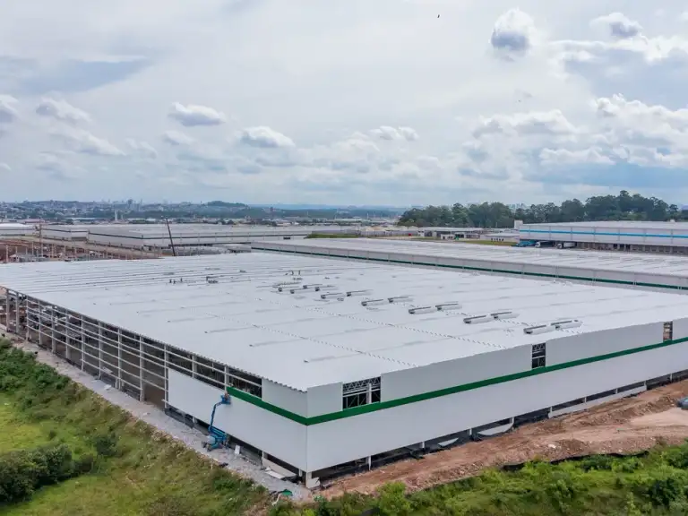 Vista aérea de galpão industrial com fachada branca e faixa verde, finalizado, rodovia ao fundo.