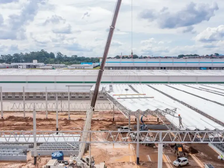 Vista aérea de galpão industrial com cobertura metálica recém-instalada, estrutura ainda parcialmente exposta.