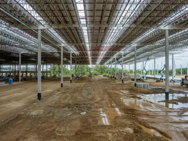 Interior de galpão industrial em construção, estrutura metálica de cobertura vista de ponta a ponta.
