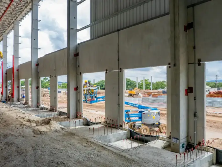 Plataforma elevatória e equipe trabalhando na estrutura metálica de um galpão industrial, piso de concreto curado.