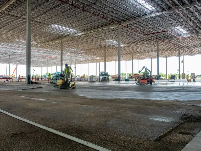 Caminhão bomba lançando concreto no piso de um galpão industrial em construção, estrutura metálica ao fundo.