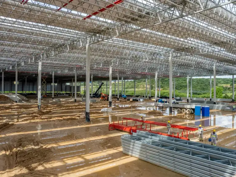 Vista ampla da montagem da estrutura metálica de cobertura de um galpão industrial, com guindastes em operação.
