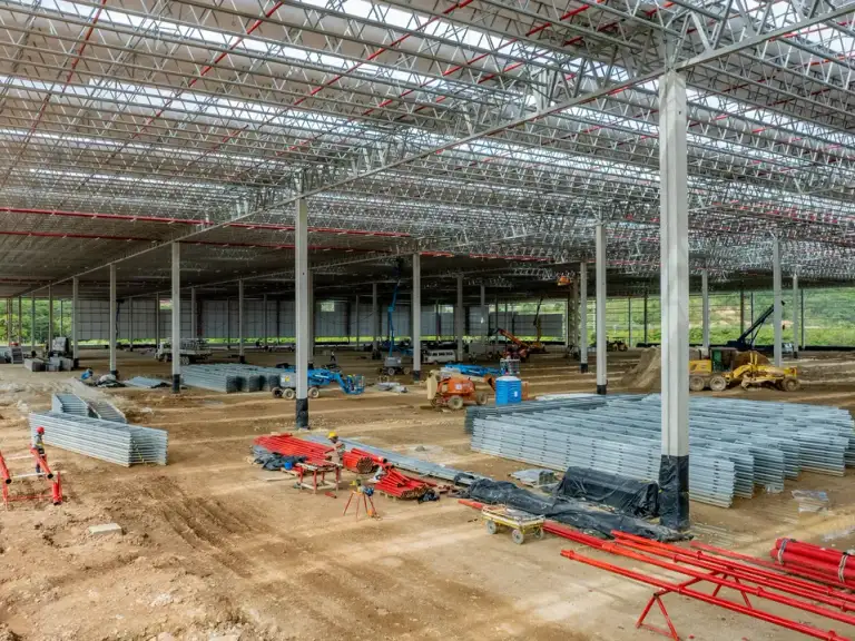 Pilhas de telhas metálicas organizadas no piso de um galpão industrial em fase de cobertura.
