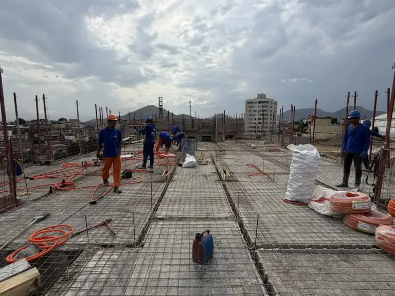 Laje de concreto armado com ferragem exposta, profissionais trabalhando no canteiro de obras.