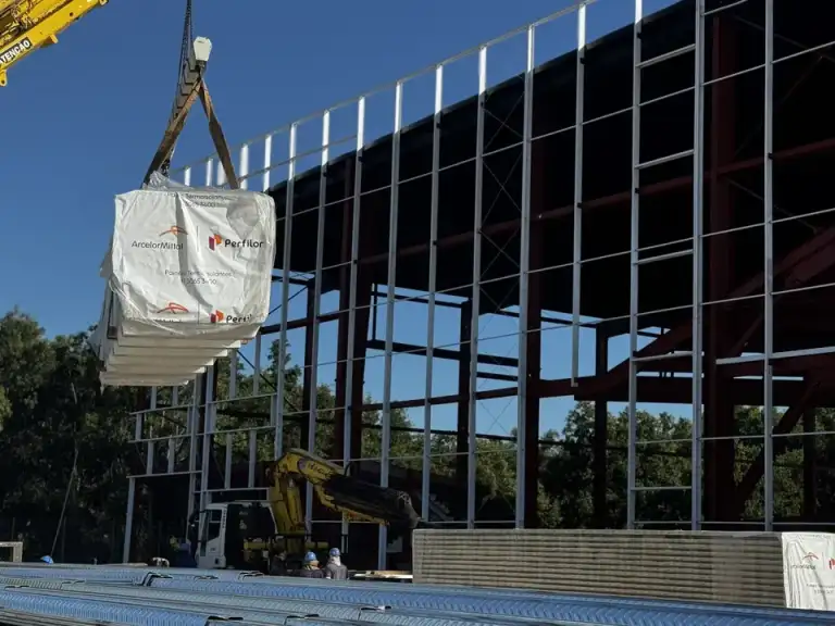 Guindaste erguendo viga metálica para montagem de estrutura de edificação em construção.