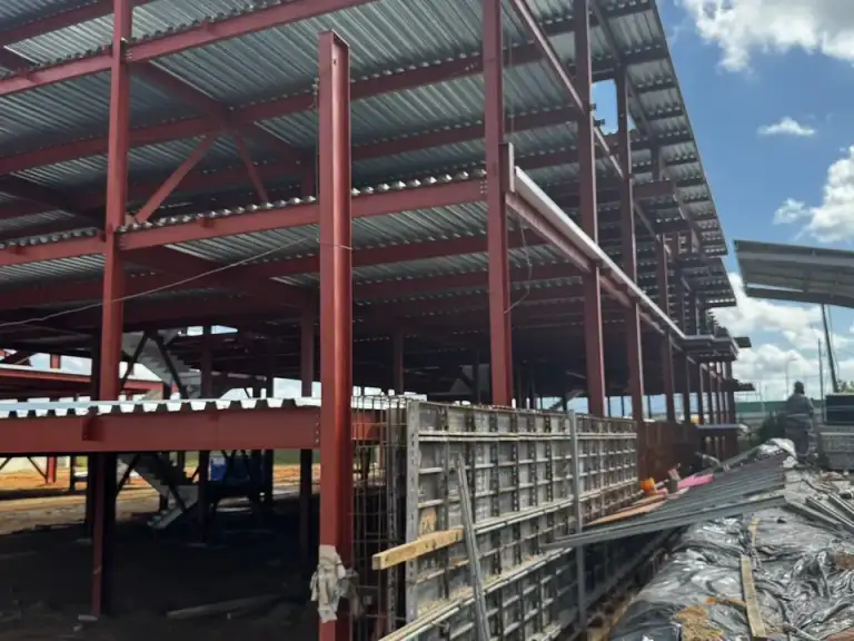Estrutura metálica vermelha de galpão em construção, cobertura parcialmente instalada.