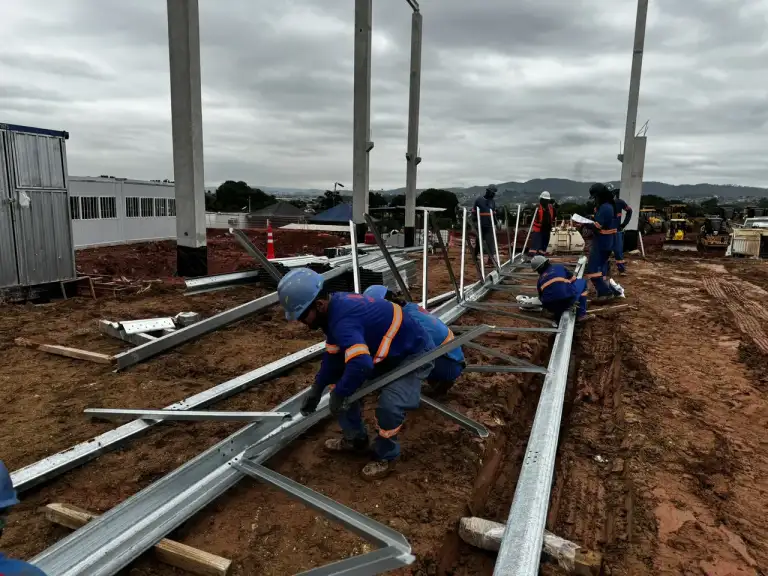 Equipe de profissionais instalando terças metálicas na cobertura de uma edificação em construção.