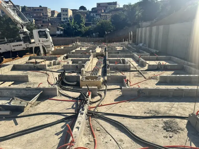 Caminhão bomba lançando concreto em fundação de edificação, área urbana ao fundo.