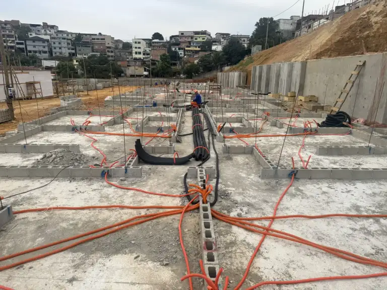 Concretagem de laje com mangotes de bombeamento, prédios residenciais ao fundo.