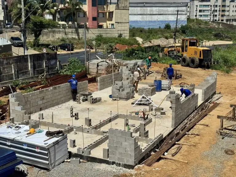 Paredes de blocos de concreto recém-erguidas em fundação de edificação, área urbana ao fundo.