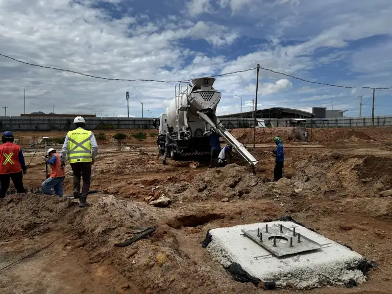 Caminhão betoneira e equipe trabalhando em fundação de edificação, com montanha ao fundo.