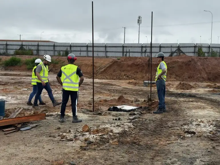 Profissionais com coletes de segurança avaliam canteiro de obras em fase inicial.