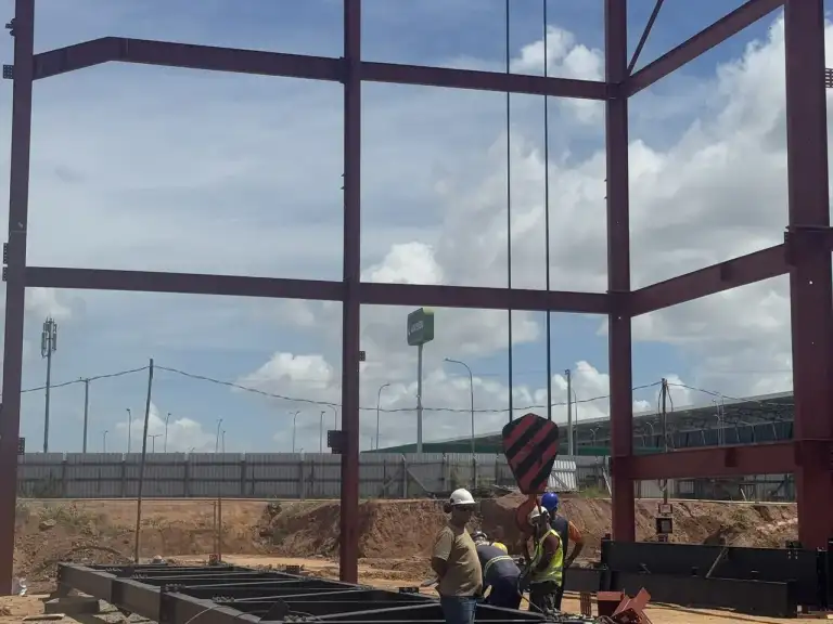Estrutura metálica vermelha de edificação em construção vista de baixo, céu azul ao fundo.
