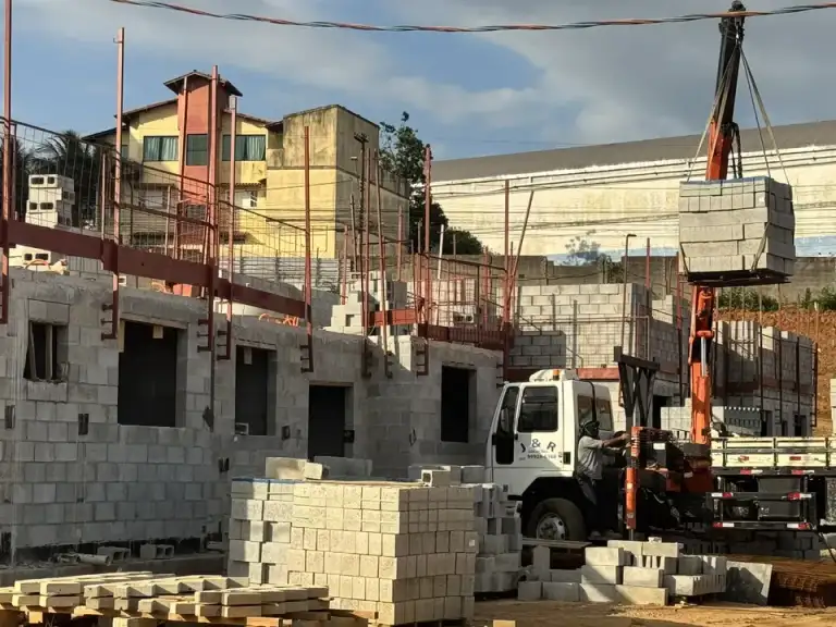 Edificações em construção em área urbana densa, guindaste e caminhão betoneira no canteiro.